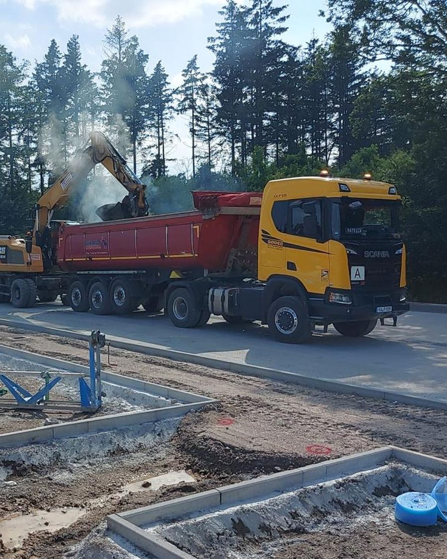 Bagger arbeitet am Godec-Kipper neben einem Straßenfertiger